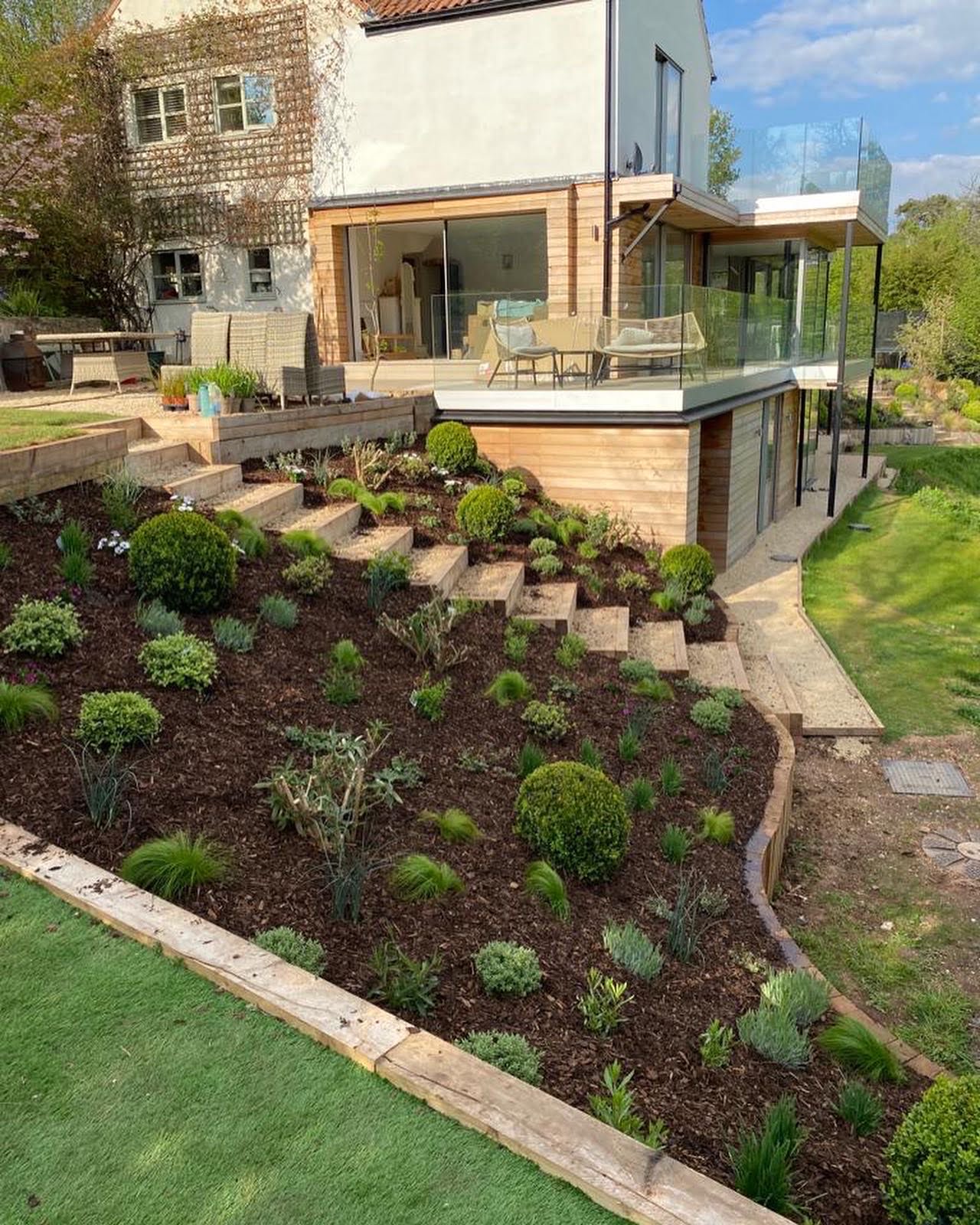 A slanted garden with numerous bushes planted and a stairway going through the middle of it.
