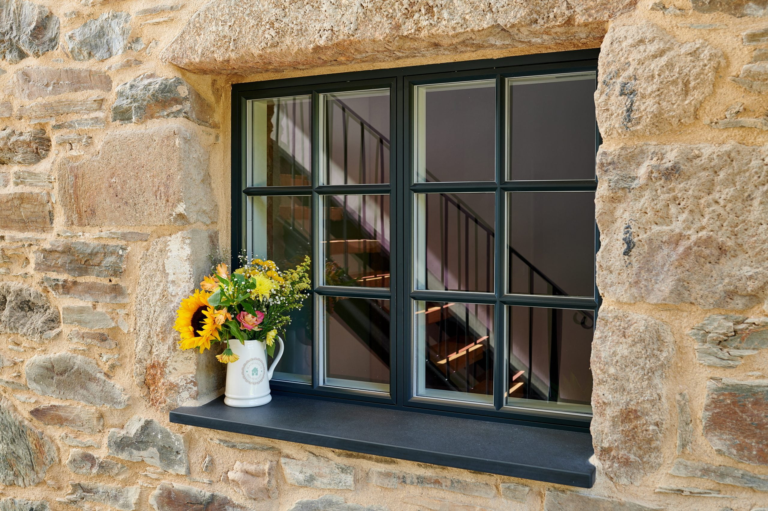 New windows, with a large windows seal with a plant pot on it that have been installed into a vintage stone building.