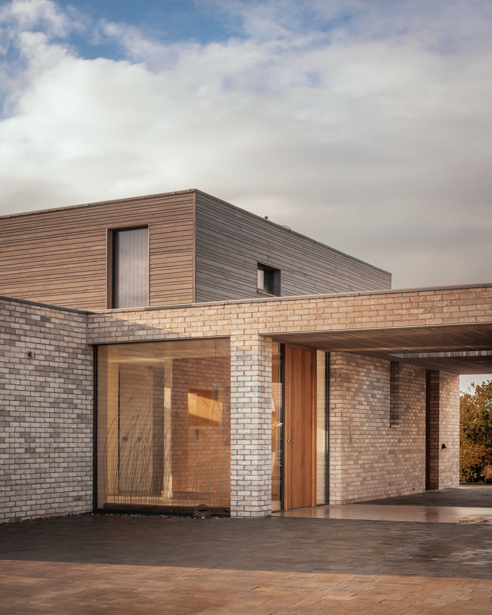 A modern house with a brick base and a wooden-cladded second floor, and a covered driveway.