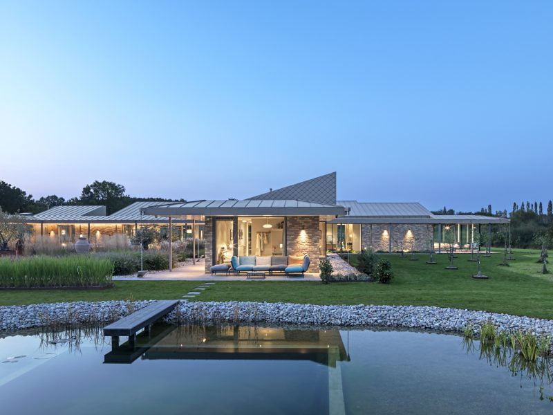 A contemporary home with a small lake that has a walkway going into it.