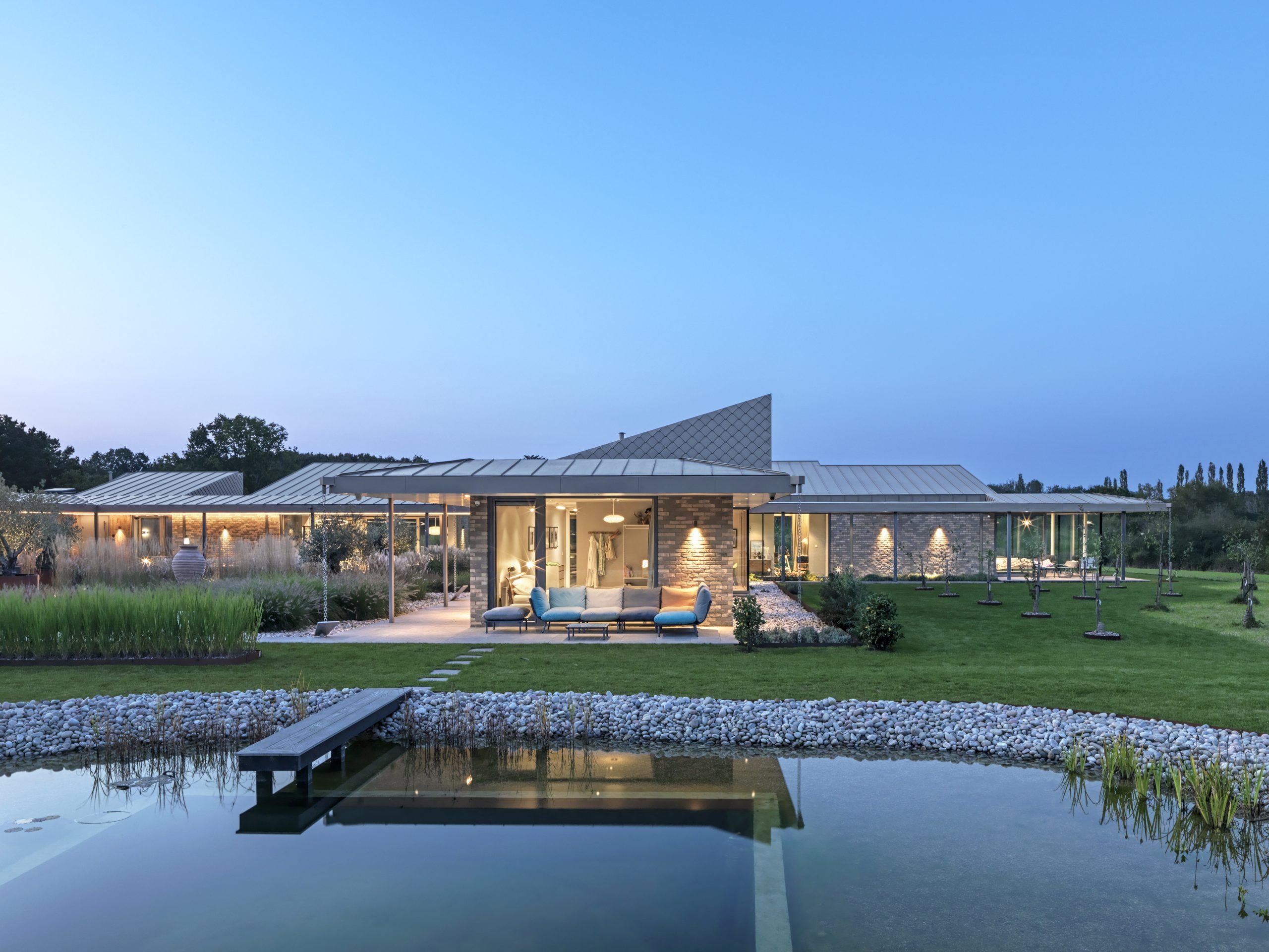 A contemporary home with a small lake that has a walkway going into it.